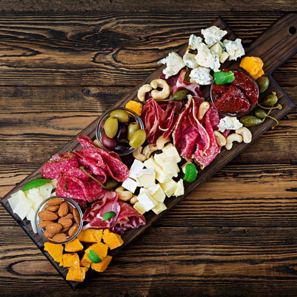 Charcuterie board with various cheeses, cured meats, olives, nuts, and sun-dried tomatoes on a wooden table.
