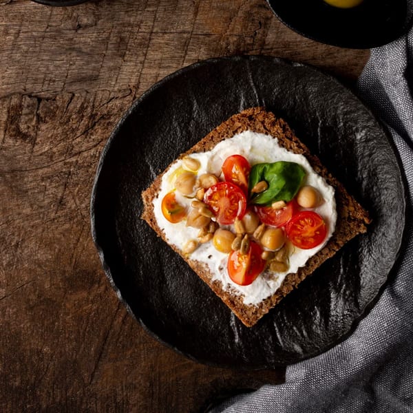 Mediterranean toast with cream cheese, cherry tomatoes, chickpeas, sunflower seeds, and basil on a dark plate.